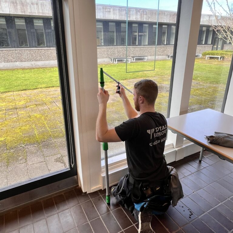 Vinduespudser renser vindue med teleskopstang mod gårdhave